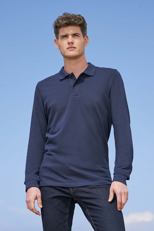 Hombre con polo azul marino de manga larga y pantalones vaqueros oscuros frente al cielo despejado.