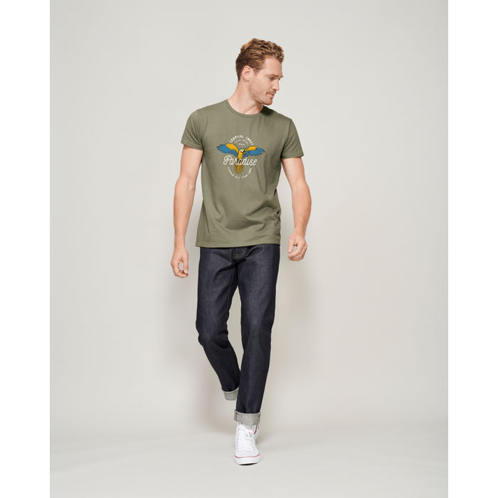 Hombre con camiseta verde caqui de algodón con estampado de loro y pantalones vaqueros oscuros.