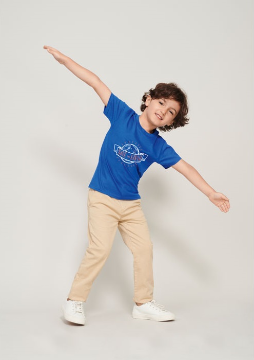Niño con camiseta azul de manga corta y pantalones beige posando con los brazos abiertos.