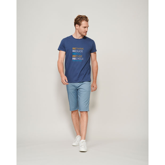 Hombre con camiseta azul marino de algodón con texto multicolor y bermudas azul claro con zapatillas blancas.