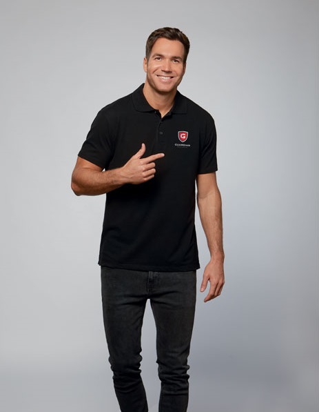 Hombre con polo negro de manga corta con logo rojo y blanco de Guardias y pantalones vaqueros oscuros.