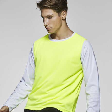 Hombre con camiseta blanca de manga larga y chaleco deportivo amarillo fluorescente.