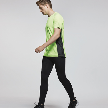 Hombre con camiseta deportiva verde y negra y mallas negras caminando.