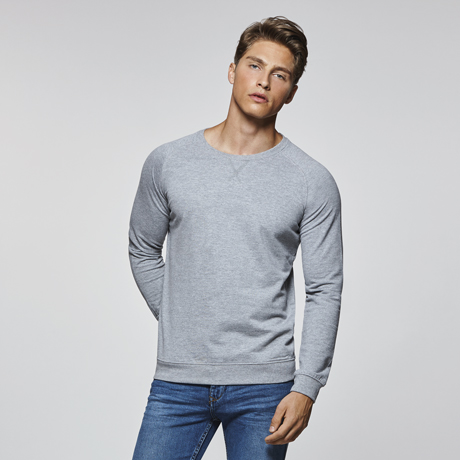 Hombre con sudadera gris de manga larga y cuello redondo combinada con vaqueros azules.