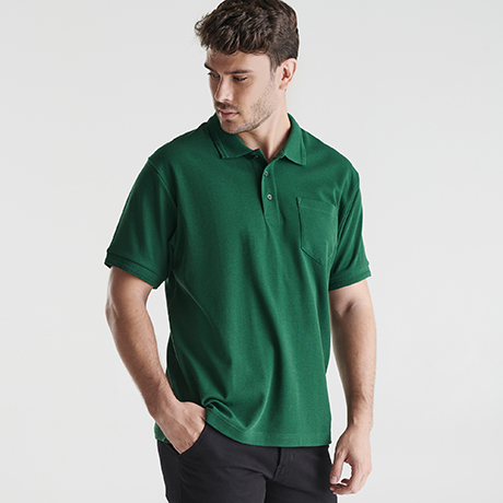 Hombre con polo verde de manga corta con bolsillo en el pecho y pantalón negro.