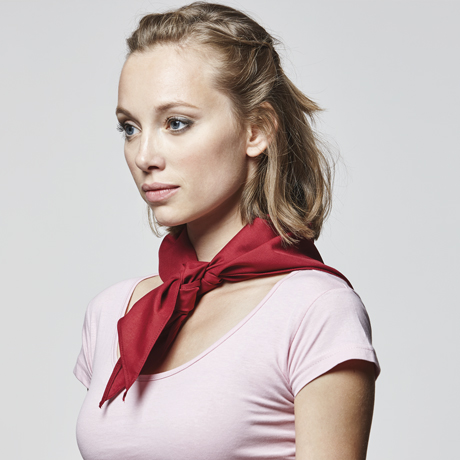 Mujer con pañuelo rojo anudado al cuello y camiseta rosa de manga corta.