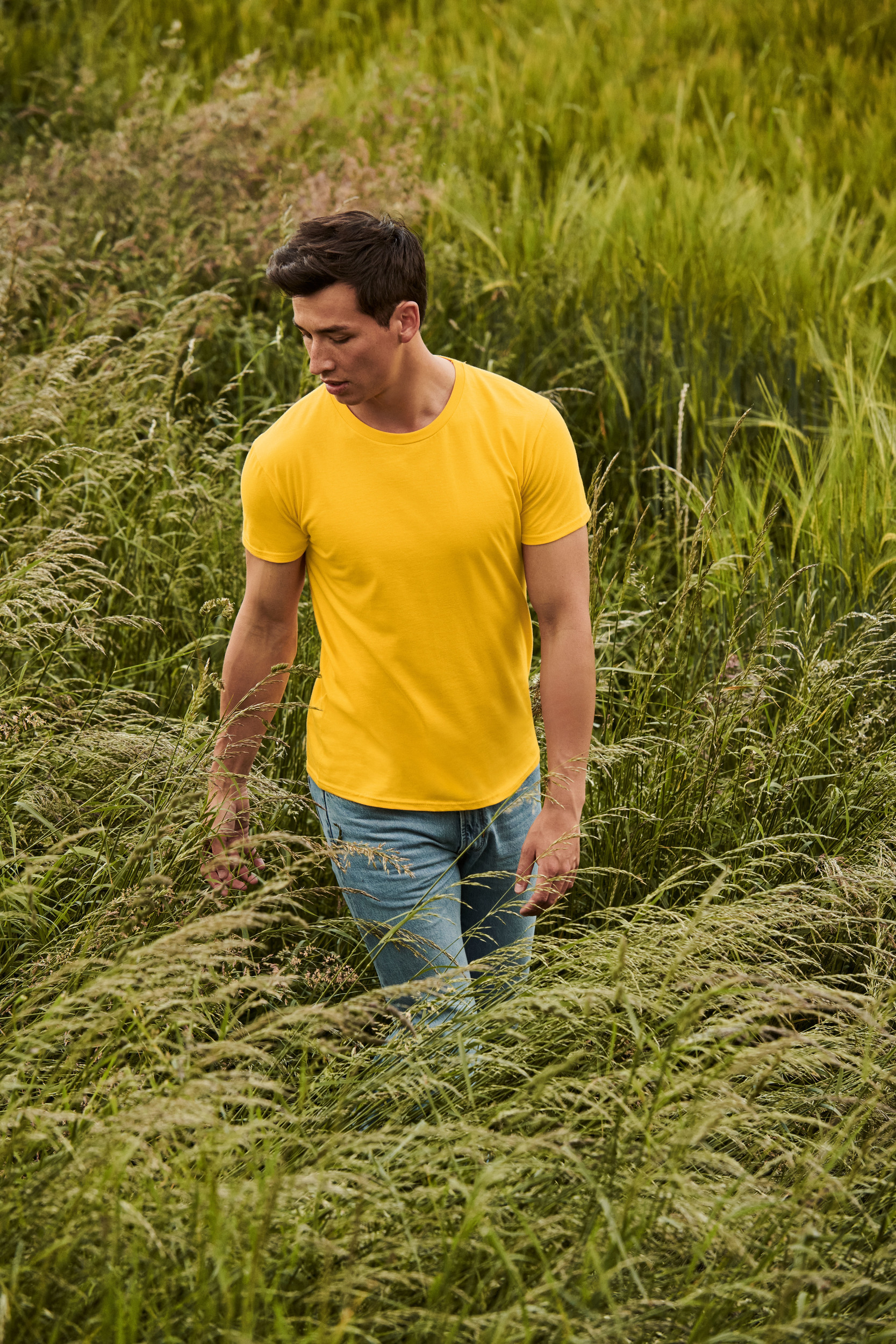Hombre con camiseta amarilla de manga corta y vaqueros claros caminando entre hierba alta.
