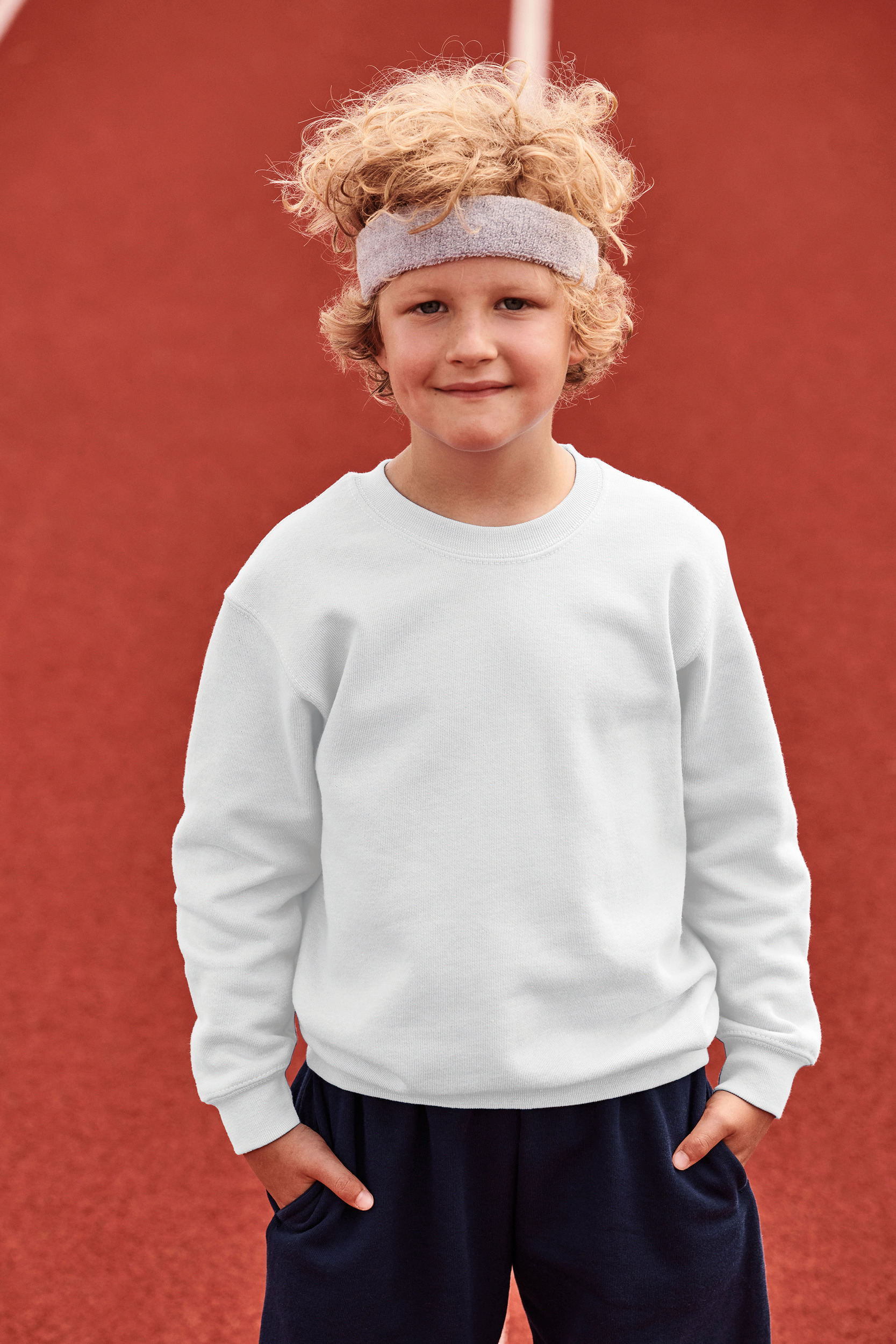 Niño con sudadera blanca y pantalones deportivos oscuros sobre pista deportiva roja.