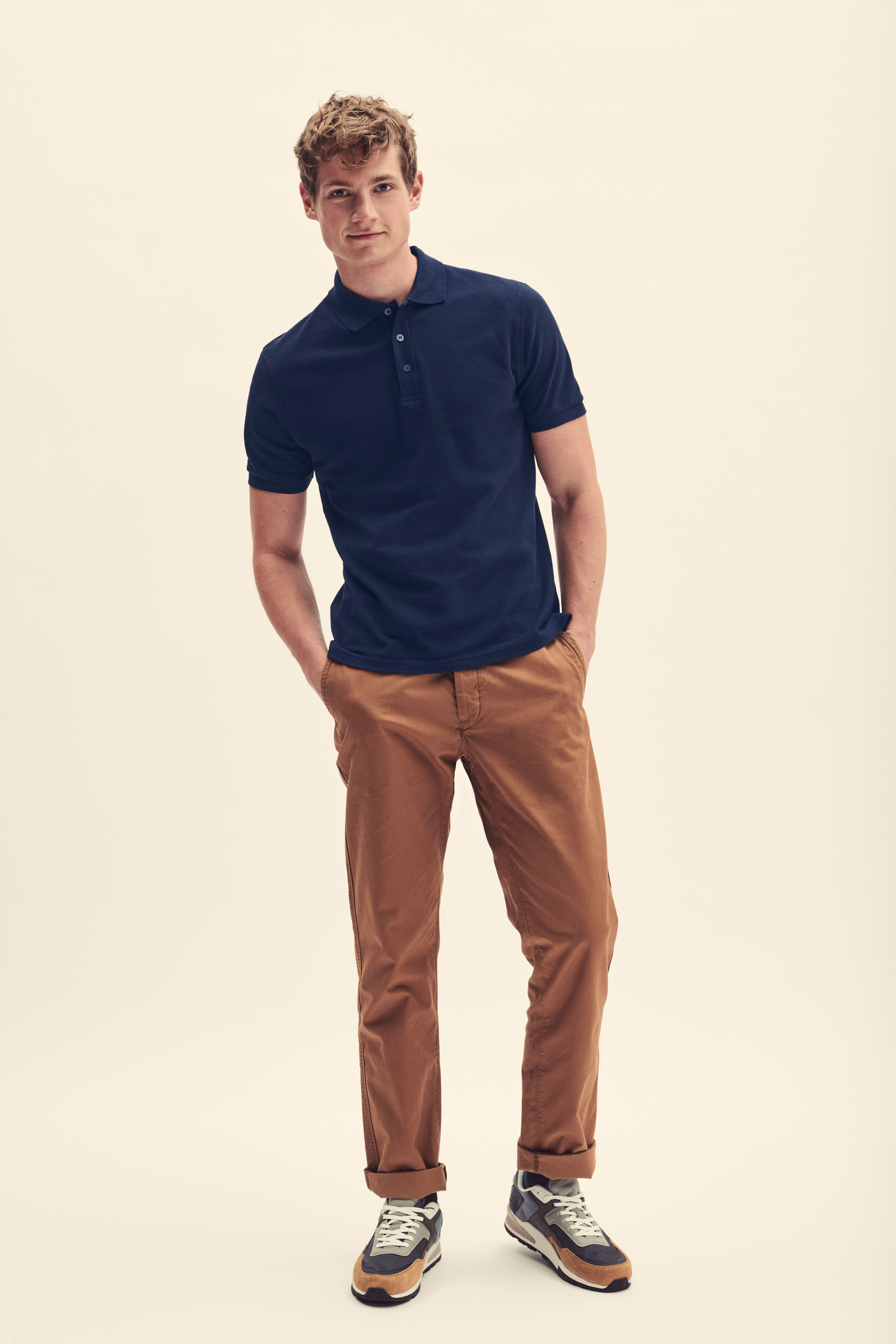 Hombre con polo azul marino de manga corta, pantalones marrones y zapatillas deportivas multicolor.