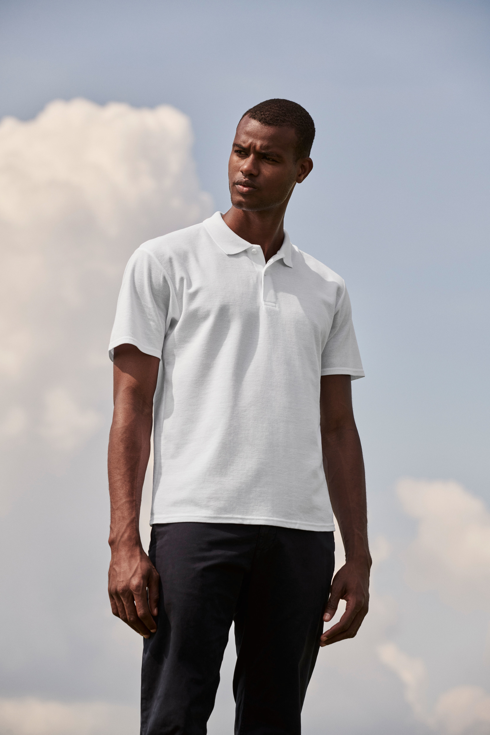 Hombre con polo blanco de manga corta y pantalones oscuros al aire libre.