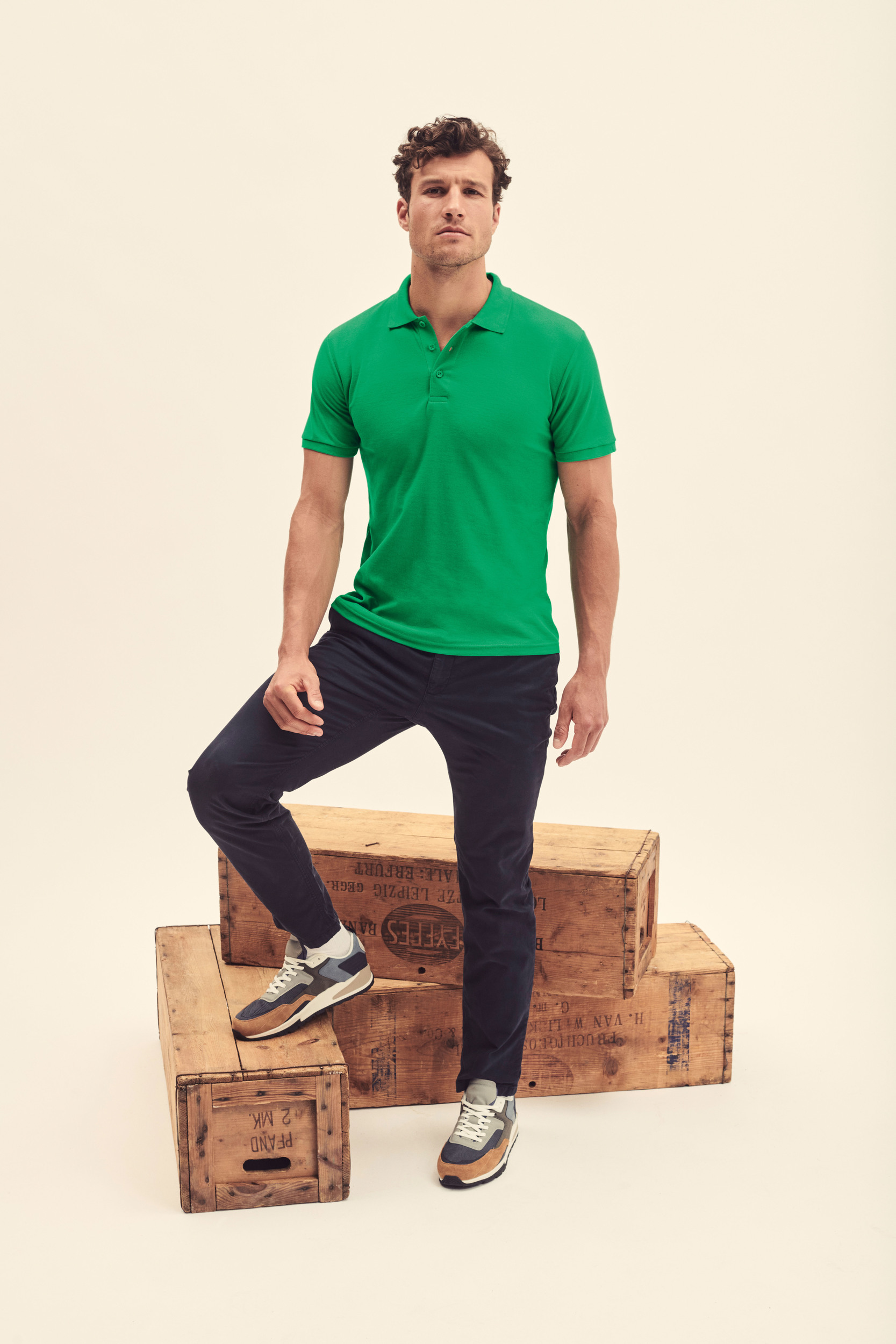 Hombre con polo verde de manga corta y pantalón azul oscuro junto a cajas de madera.