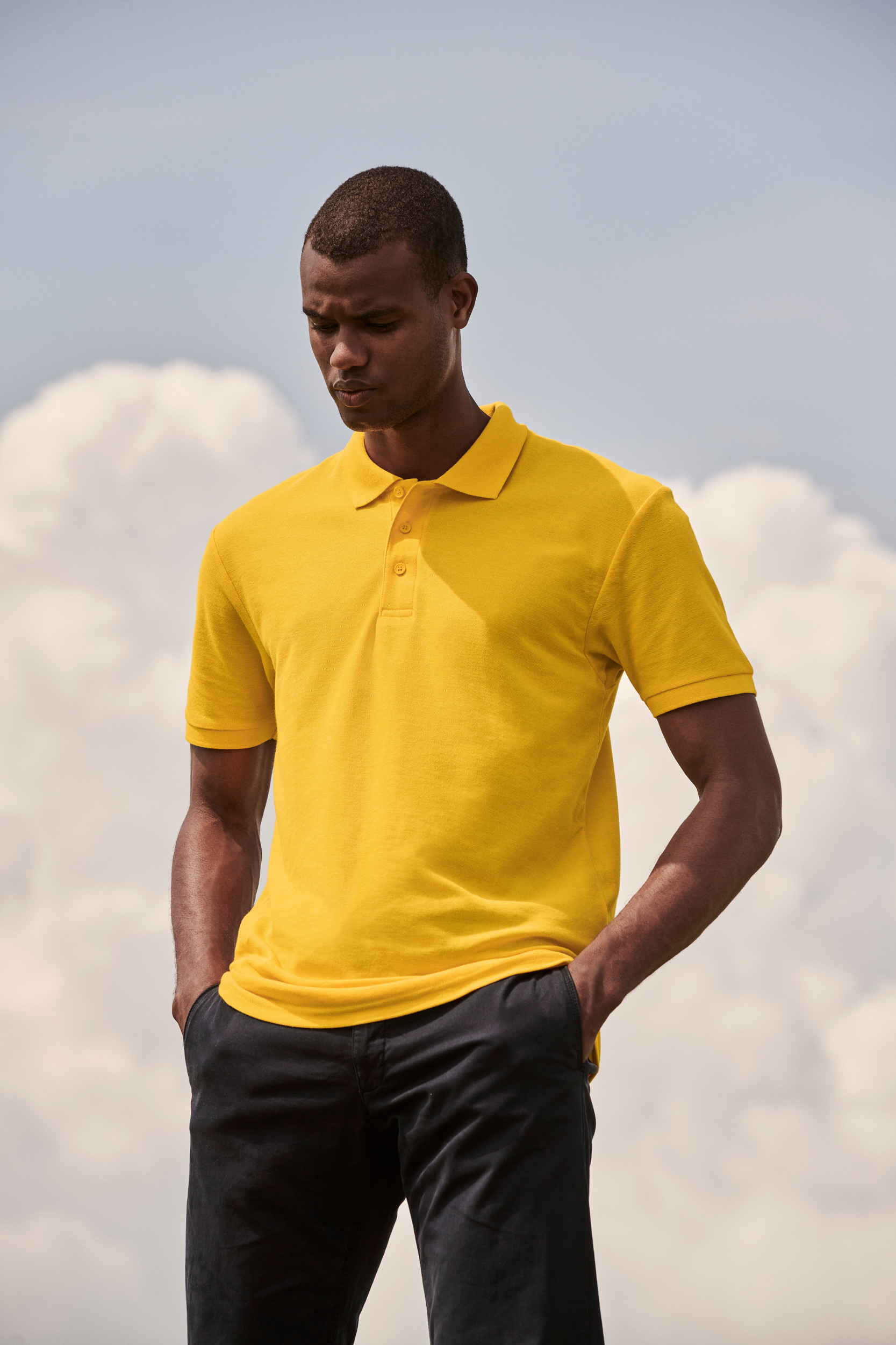 Hombre con polo amarillo de manga corta y pantalones oscuros al aire libre.